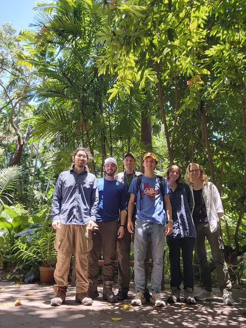 Six lab members under palms and tropical trees in a botanic garden