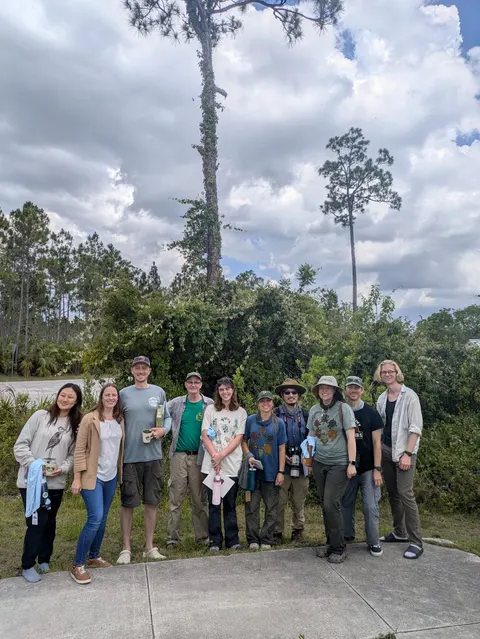 The lab and collaborators in front of tall pine trees in south Florida