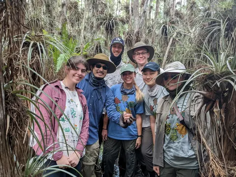 Lab members standing in a cypress swamp full of air plants, one holding a small snake